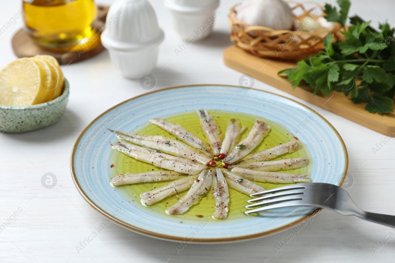 Photo of Tasty pickled anchovies with spices on white wooden table, closeup