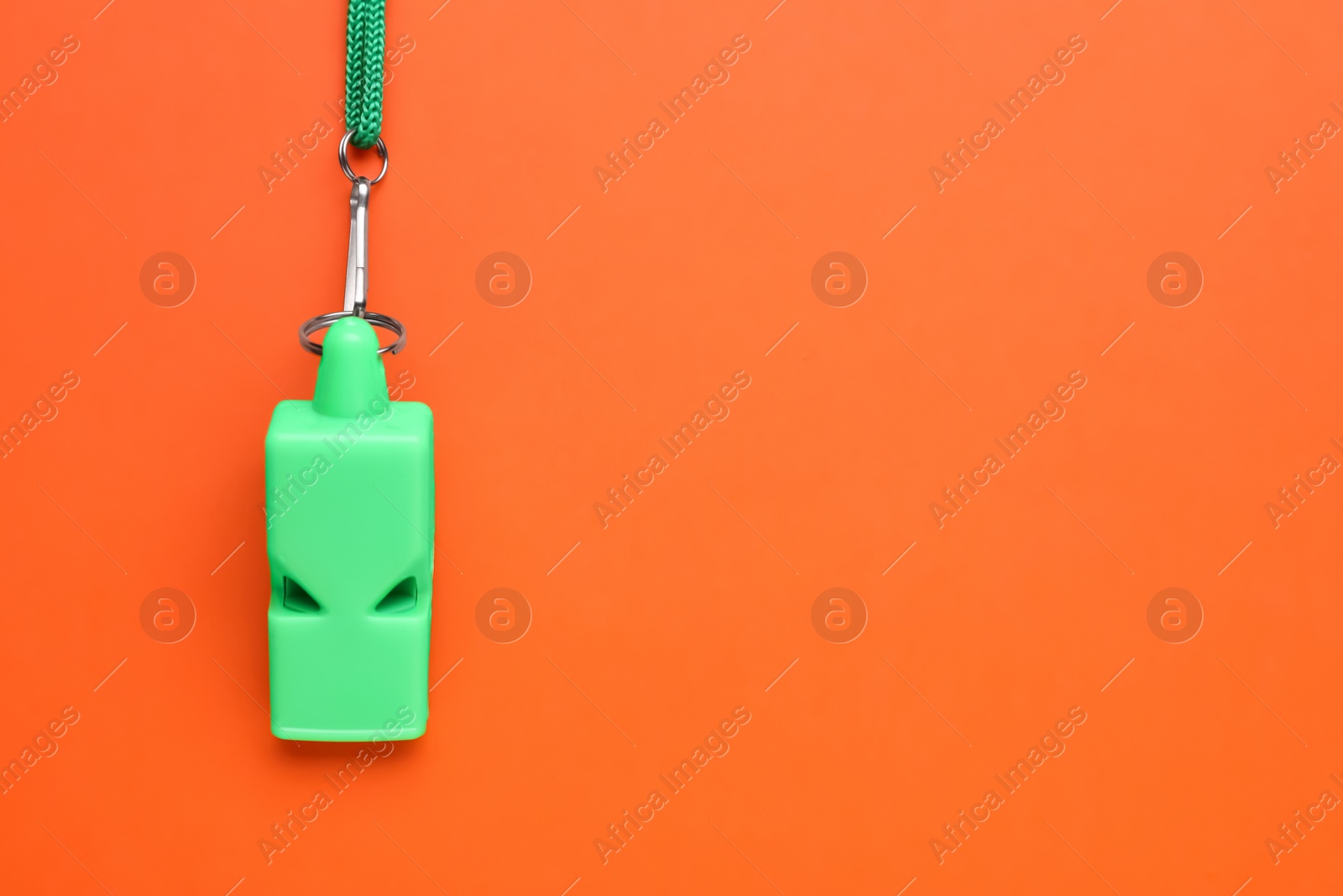 Photo of One green whistle with cord on orange background, top view. Space for text