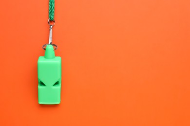 Photo of One green whistle with cord on orange background, top view. Space for text