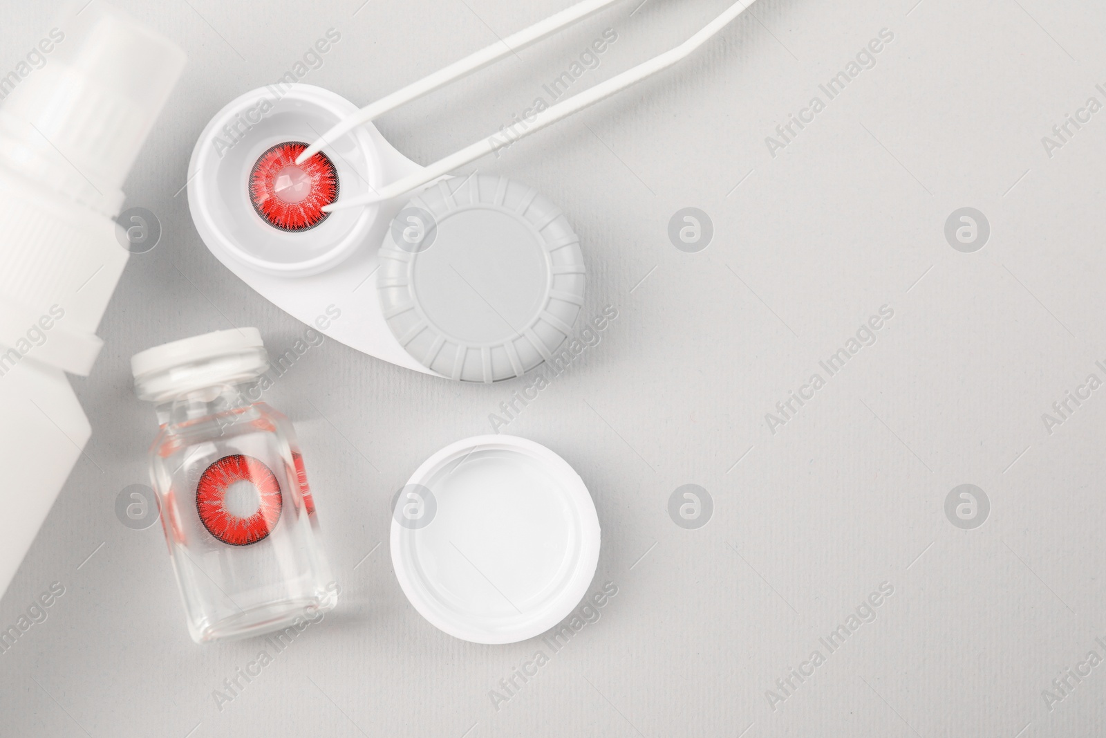 Photo of Case with red contact lenses, bottle of solution and tweezers on light grey background, flat lay. Space for text