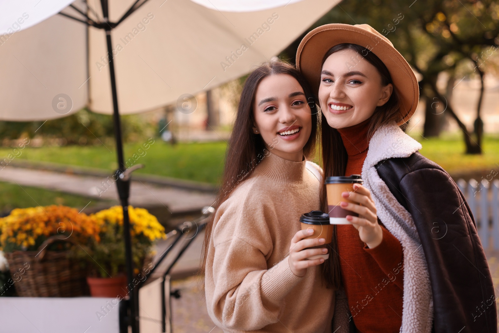 Photo of Happy friends with paper cups of coffee outdoors, space for text