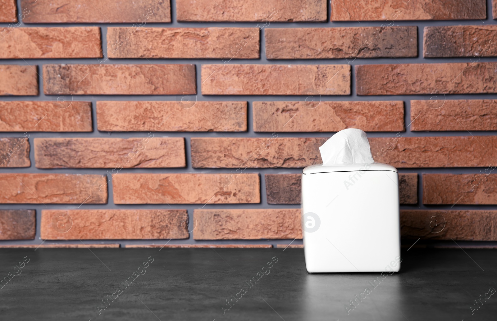 Photo of Napkin holder with paper serviettes on table against brick wall. Space for text