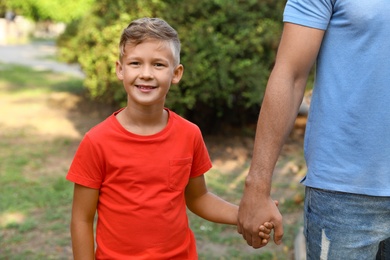 Photo of Little boy and his father holding hands outdoors. Family weekend