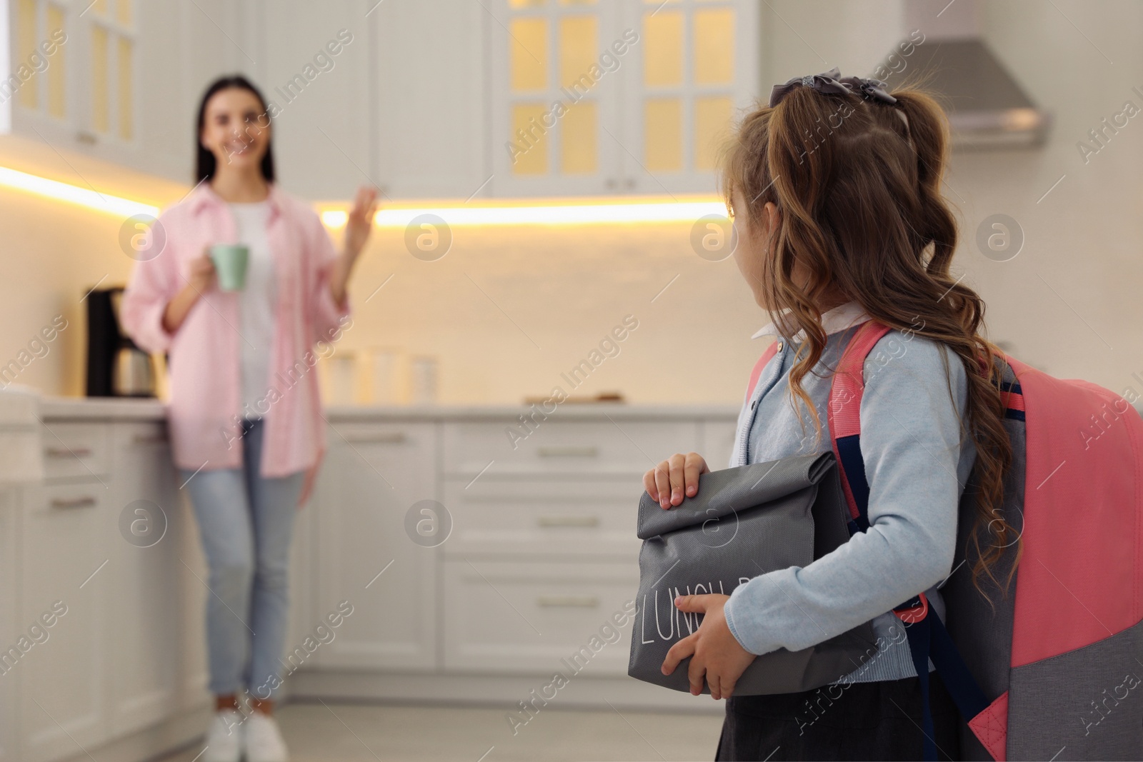 Photo of Little girl with lunch bag and mother in kitchen. Getting ready for school