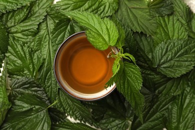 Photo of Cup of aromatic nettle tea on fresh green leaves, top view