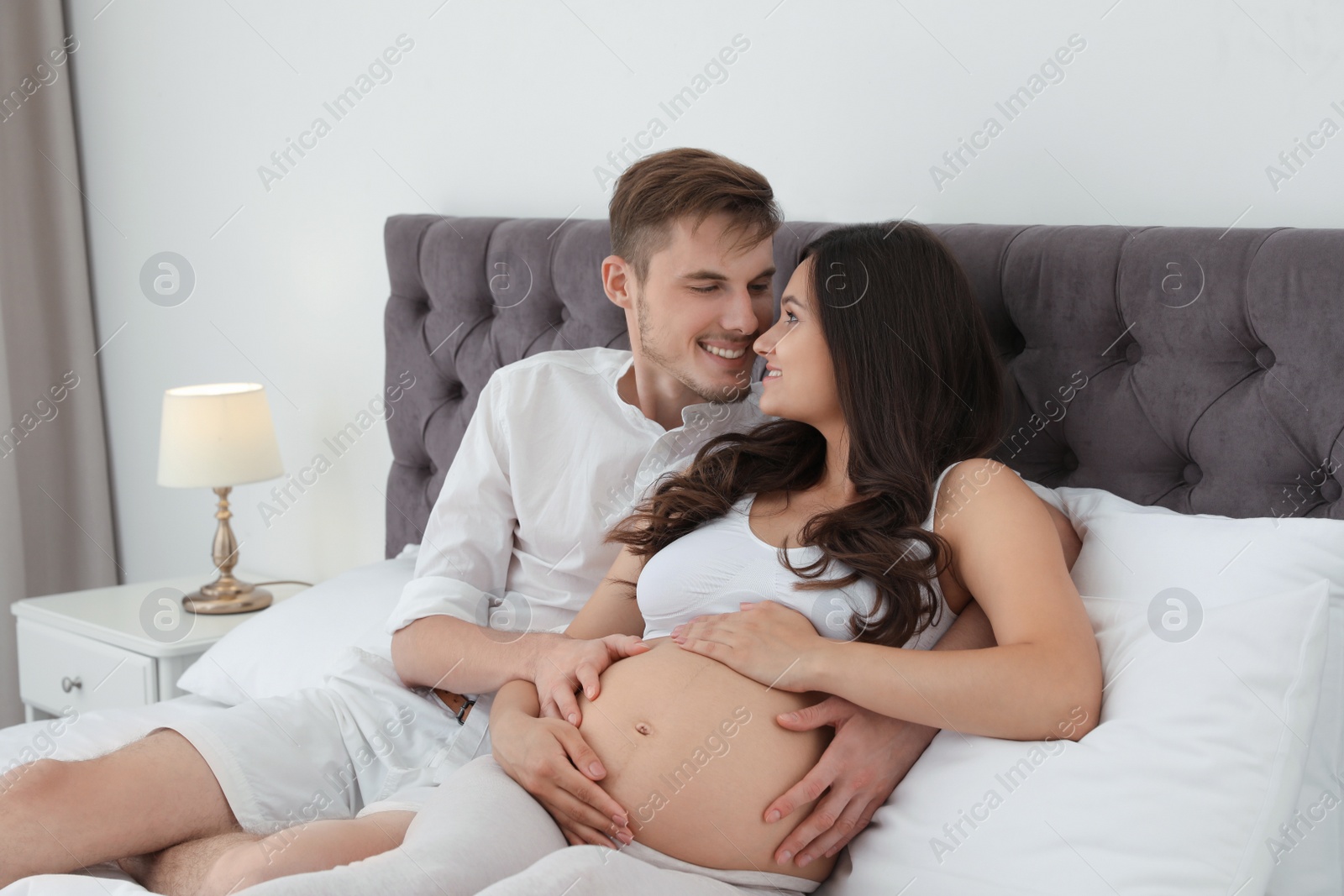 Photo of Young husband and his pregnant wife lying in bed at home