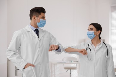 Photo of Doctors with protective masks greeting each other by bumping elbows instead of handshake in clinic