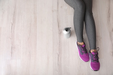 Photo of Woman in sportswear with bottle of water sitting on floor indoors, top view. Space for text