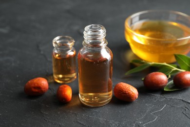Photo of Jojoba oil and seeds on dark grey table