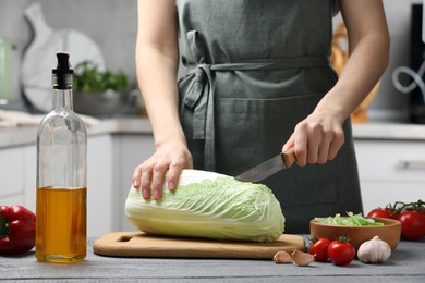 Photo of Woman cutting fresh chinese cabbage at grey wooden table in kitchen, closeup