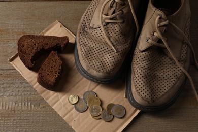 Photo of Poverty. Old shoes, coins, pieces of bread and cardboard sheet on wooden table, above view