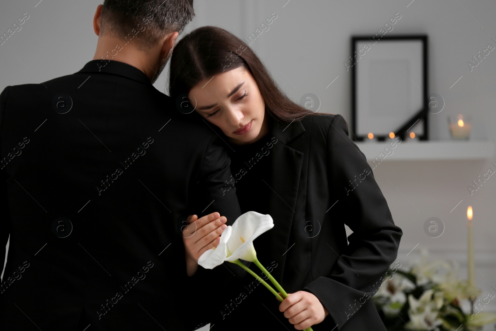Photo of Sad couple with calla lily flowers mourning indoors, space for text. Funeral ceremony