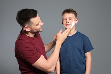Photo of Dad applying shaving foam on son's face, grey background