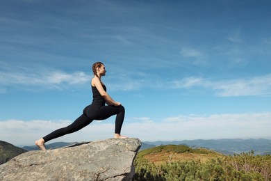 Photo of Beautiful young woman stretching on rock in mountains