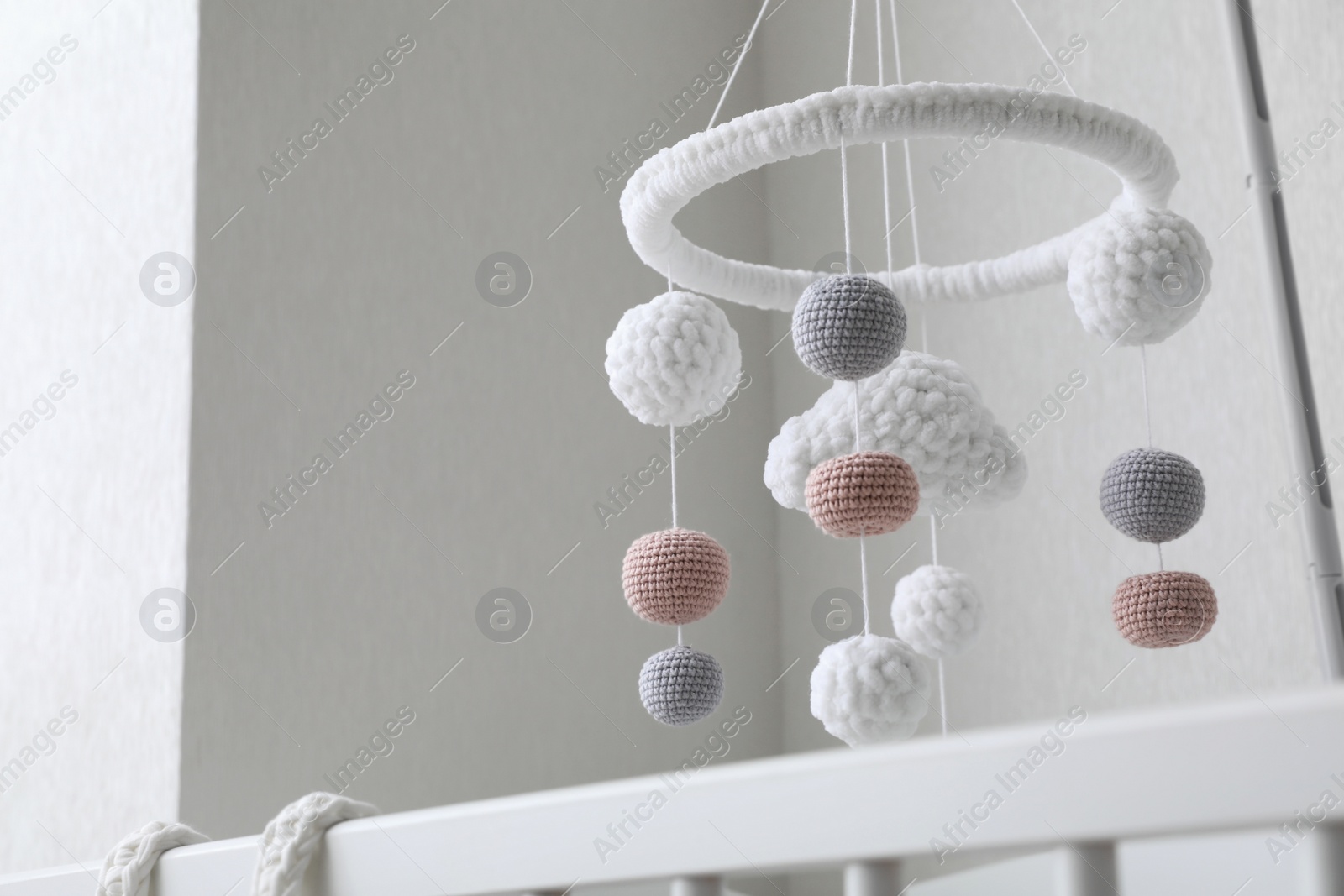 Photo of Modern baby mobile under crib near beige wall in room, low angle view