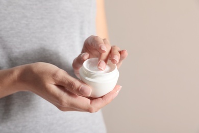 Photo of Young woman holding jar of cream on light background, closeup. Space for text