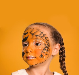 Photo of Cute little girl with face painting on orange background