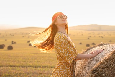 Photo of Happy hippie woman near hay bale in field, space for text
