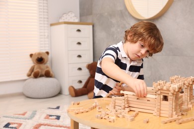 Photo of Little boy playing with wooden construction set at table in room, space for text. Child's toy