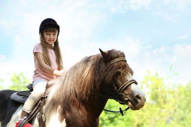 Photo of Cute little girl riding pony outdoors on sunny day