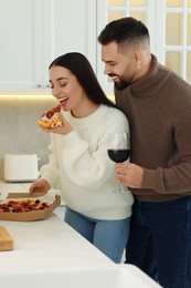Photo of Happy young couple eating pizza and drinking wine in kitchen