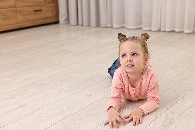 Photo of Cute little girl lying on warm floor at home, space for text. Heating system