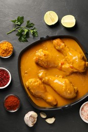 Photo of Tasty chicken curry and ingredients on black textured table, flat lay