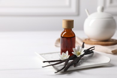 Photo of Vanilla pods, essential oil and flowers on white wooden table, space for text