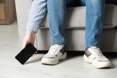 Photo of Man taking dropped smartphone from floor indoors, closeup. Device repairing