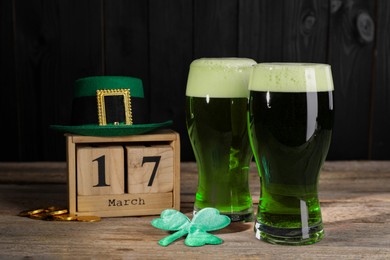 Photo of St. Patrick's day celebrating on March 17. Green beer, block calendar, leprechaun hat, gold coins and decorative clover leaf on wooden table