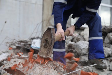 Photo of Man breaking brick with sledgehammer outdoors, selective focus