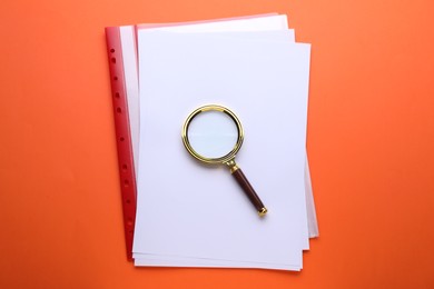 Photo of Magnifying glass and folder with paper sheets on orange background, top view