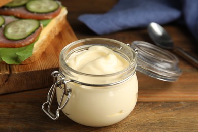 Photo of Jar of delicious mayonnaise near fresh sandwich on wooden table