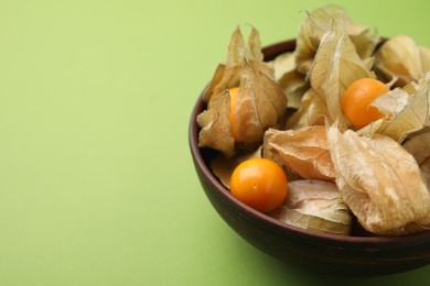 Photo of Ripe physalis fruits with calyxes in bowl on green background, closeup. Space for text