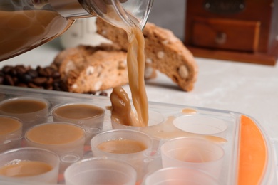 Photo of Pouring coffee drink into ice cube tray on table, closeup