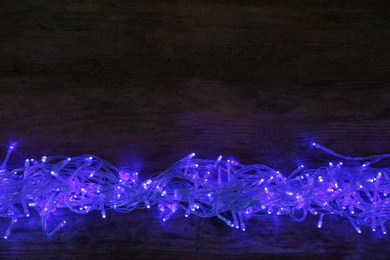 Photo of Blue Christmas lights on wooden background, top view. Space for text
