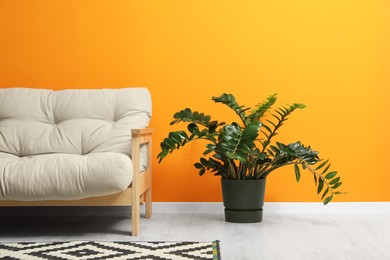 Photo of Stylish beige sofa, patterned rug and beautiful houseplant near orange wall indoors. Interior design