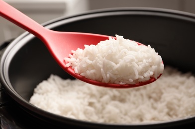 Photo of Spoon with tasty hot rice over cooker, closeup
