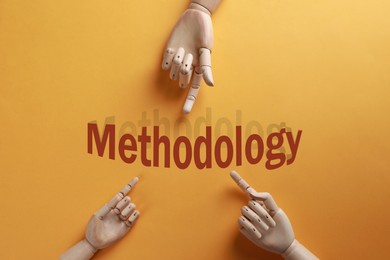 Image of Wooden mannequin hands pointing at word Methodology on orange background, flat lay