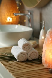 Photo of Spa composition. Rolled towels, burning candle and Himalayan salt lamp on countertop in bathroom