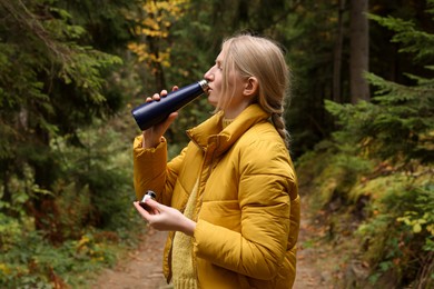 Photo of Young woman drinking hot beverage from thermo bottle in autumn forest