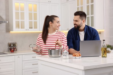 Photo of Happy lovely couple using laptop while cooking in kitchen
