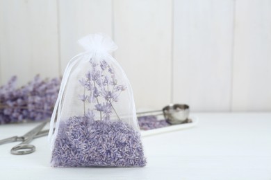 Photo of Scented sachet with dried lavender flowers on white table, space for text