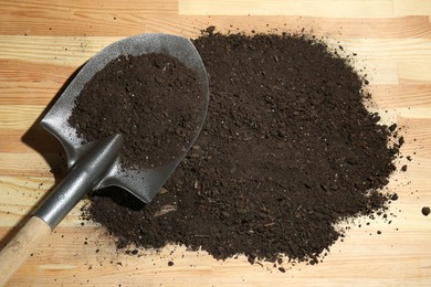 Photo of Metal shovel and soil on wooden surface, top view