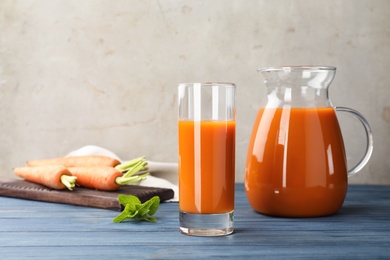 Glass and jug of carrot drink on table against light background, space for text