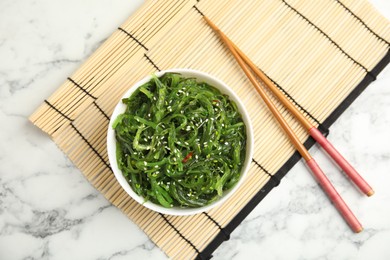 Photo of Japanese seaweed salad served on white marble  table, flat lay