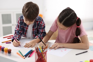 Photo of Happy brother and sister drawing at white table in room