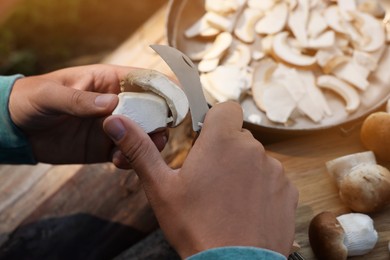 Photo of Man cutting mushroom with knife at wooden table, closeup