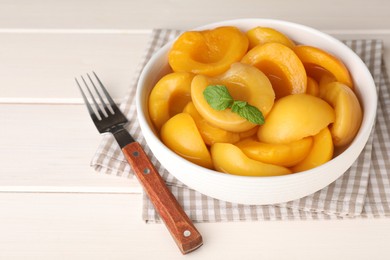 Photo of Canned peach halves and fork on white wooden table