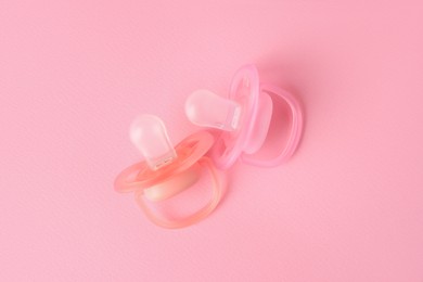 Photo of New baby pacifiers on pink background, flat lay